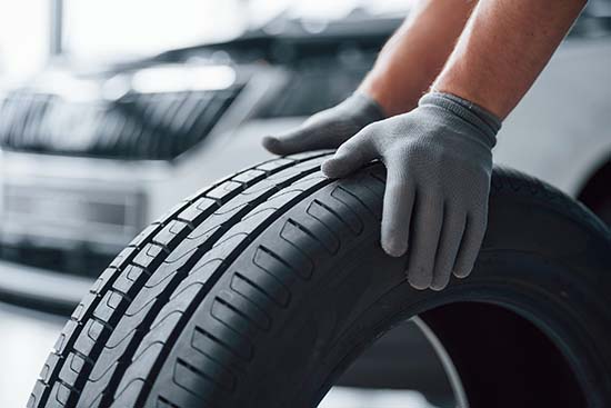 Hands only. Mechanic holding a tire at the repair garage. Replacement of winter and summer tires